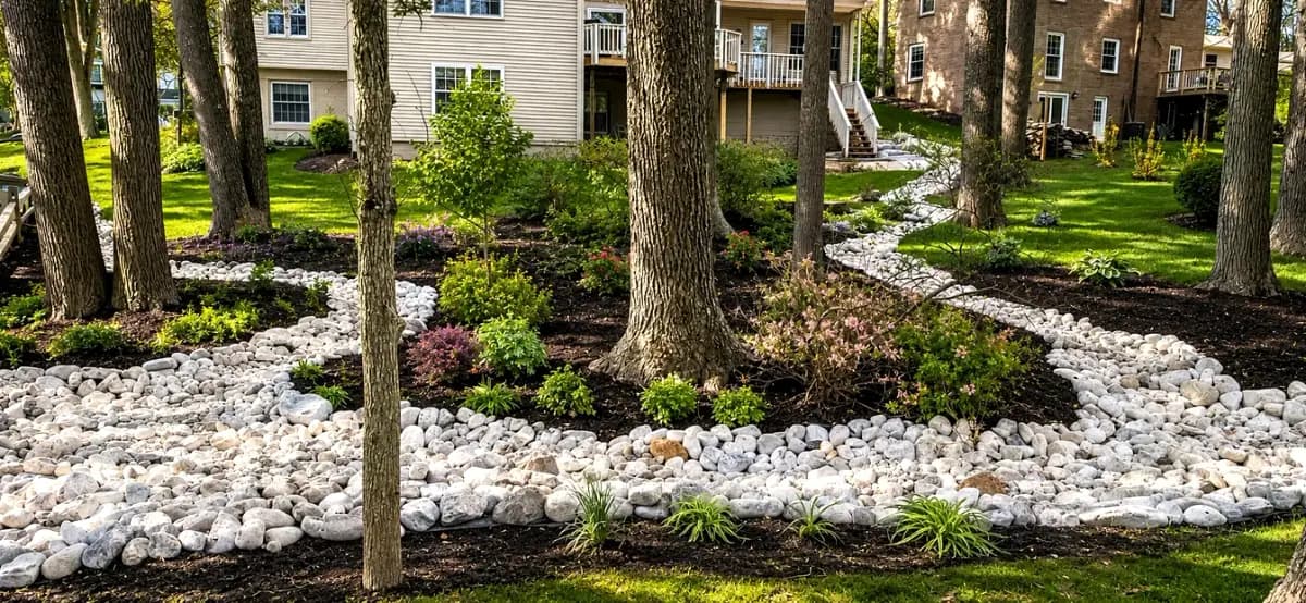 White river-rock drainage swale channeling stormwater between mulched plantings