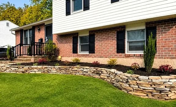 Natural stacked-stone retaining wall bordering a manicured lawn and brick home