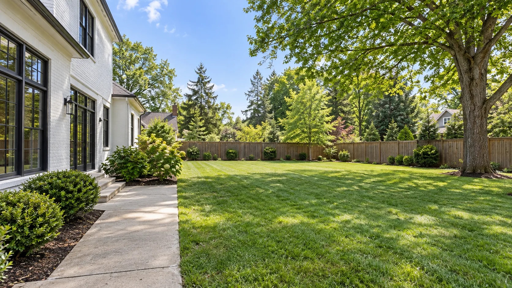 A residential backyard before redesign — an open lawn with a bare patio and sparse planting.