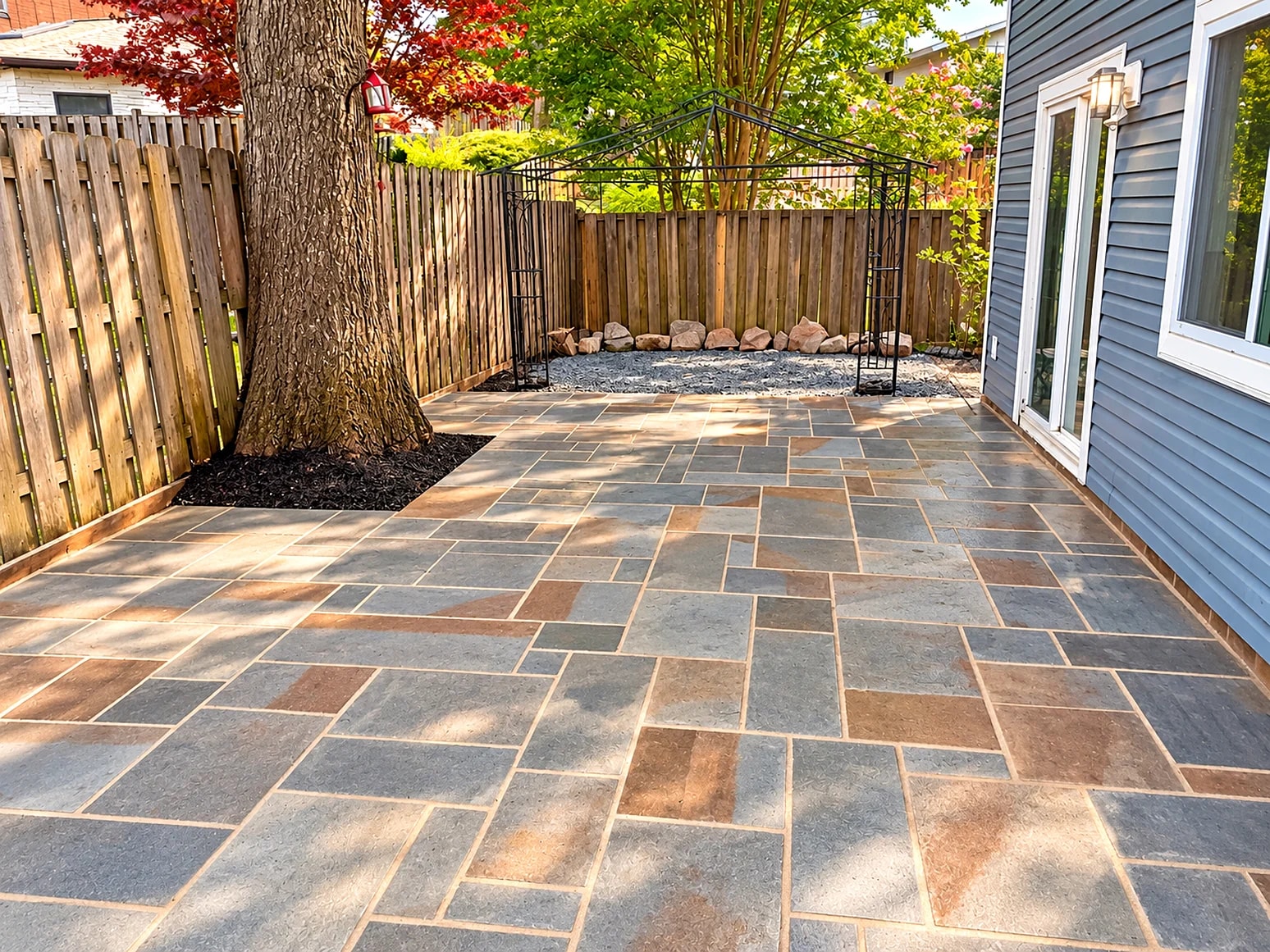 Large-format pattern-cut flagstone patio beneath a red Japanese maple, enclosed by a wood privacy fence