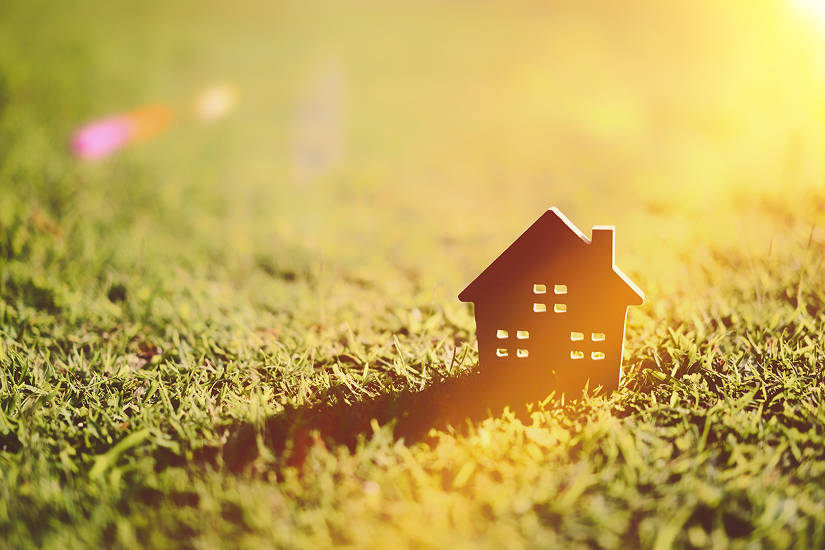 Small model home on green grass with sunlight abstract background.